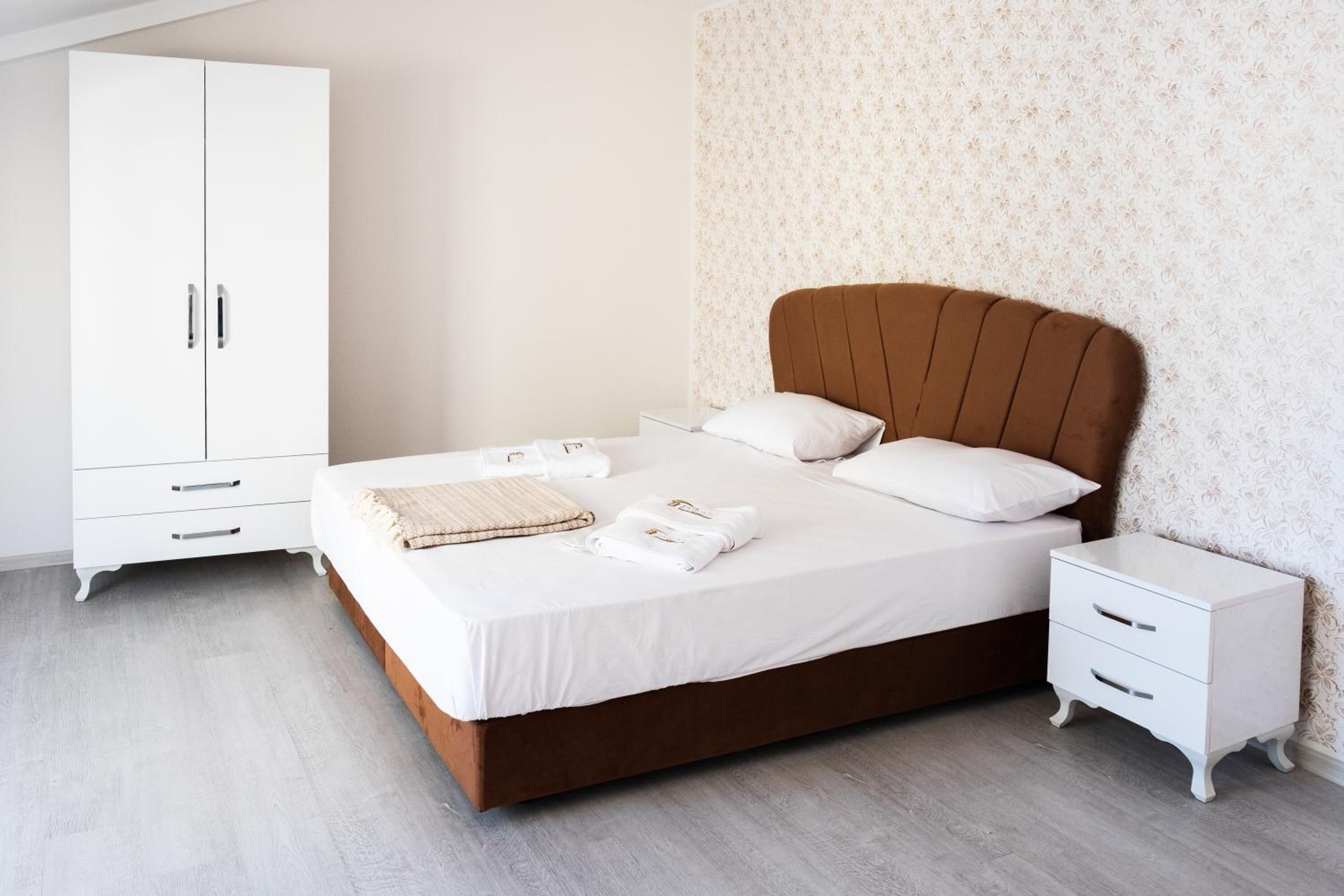 Ein Schlafzimmer mit einem Bett, weißen Nachttischen, einem Kleiderschrank und einem gemusterten Wandpapier.