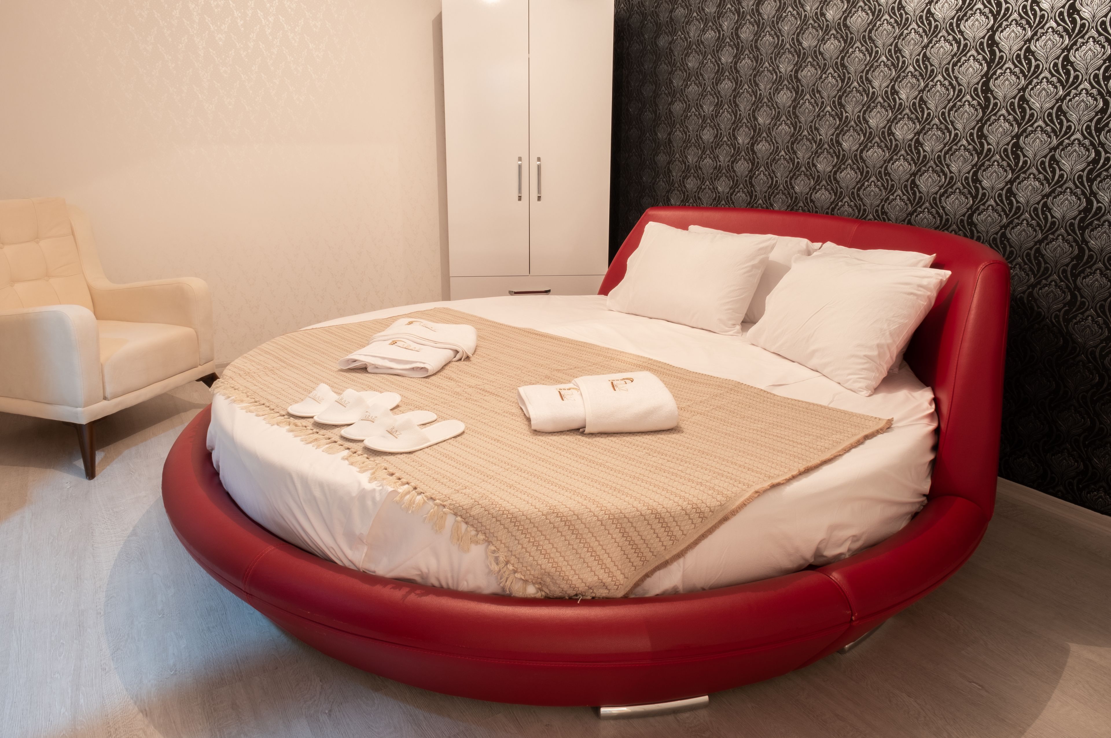 A modern bedroom with a circular bed, a white wardrobe, and a patterned wall.