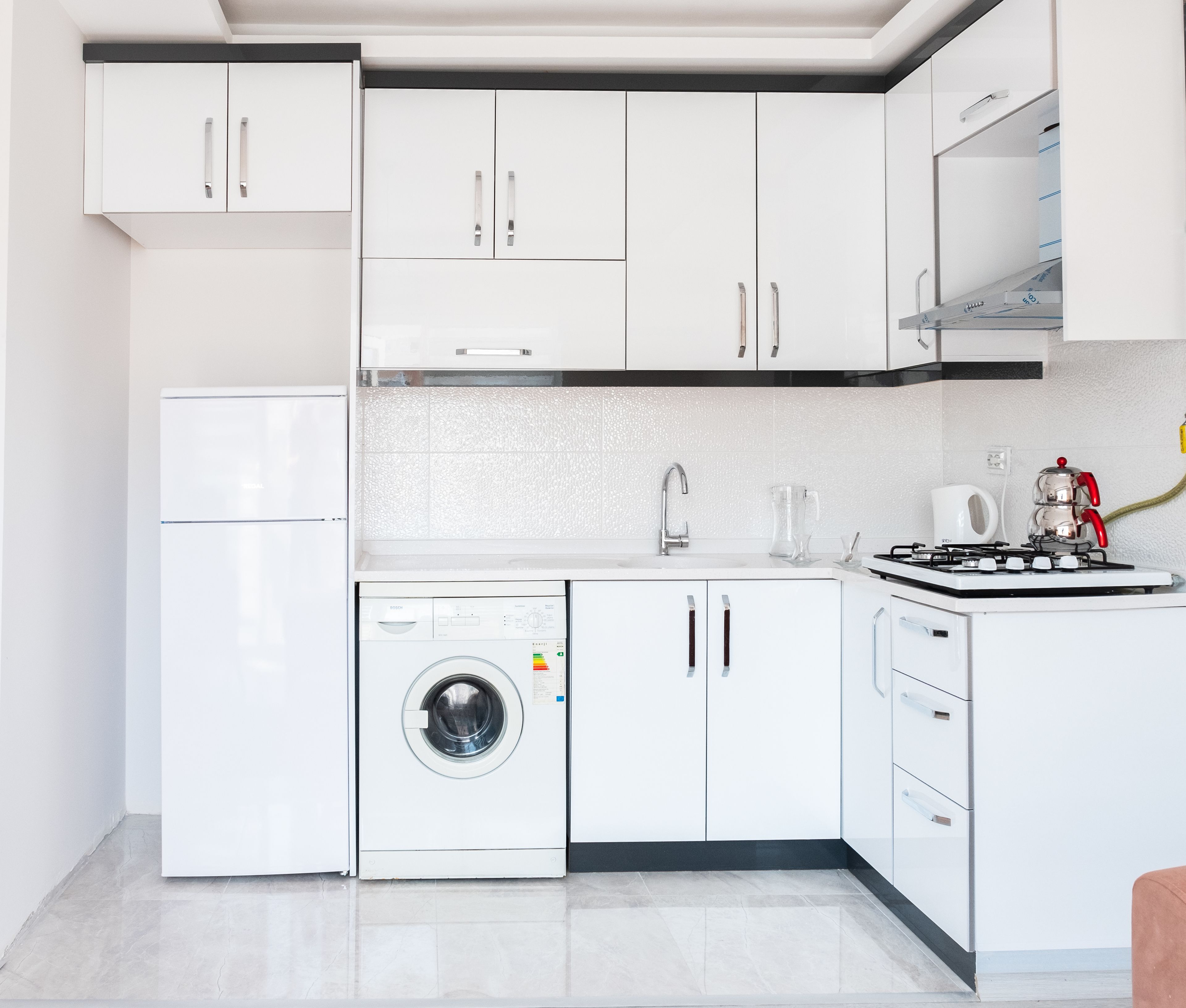 A modern kitchen with white cabinetry, a built-in washing machine, a gas stove, and a sink.