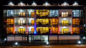 A multi-story hotel with a modern design, featuring balconies, large windows, and a well-lit facade.
