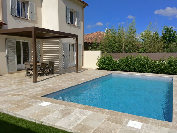 A swimming pool with a pergola and outdoor furniture, surrounded by a well-maintained lawn and hedges.