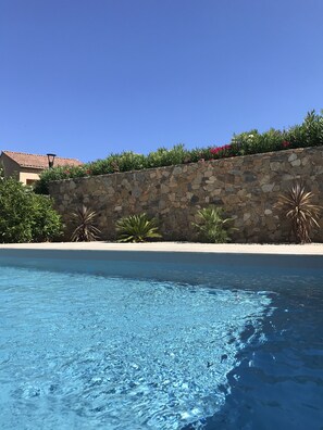 A clear blue pool with a stone wall and plants in the background.