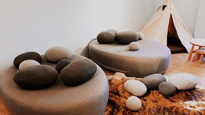 Ein Zimmer mit zwei Sitzbereichen, einem kleinen Tisch, einem Holzstuhl und einer Tipizelt-Struktur.