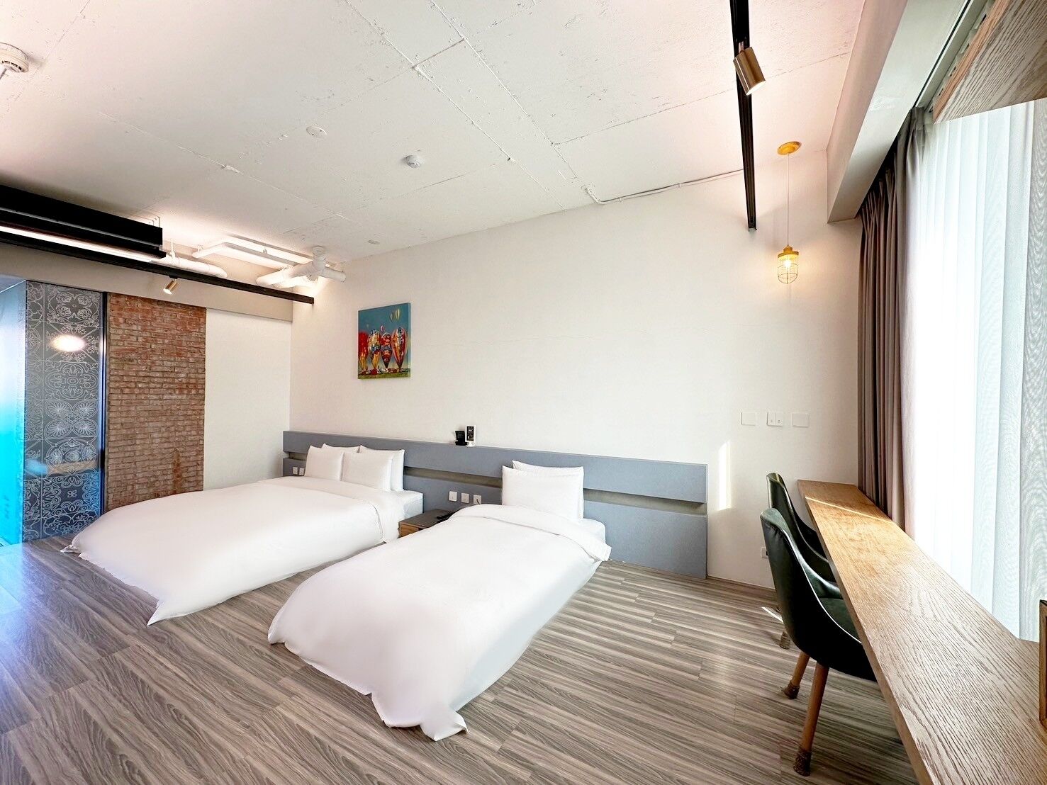 Ein Hotelzimmer mit zwei Betten, einem Schreibtisch, einem Fenster mit Vorhängen und einem Bild an der Wand.