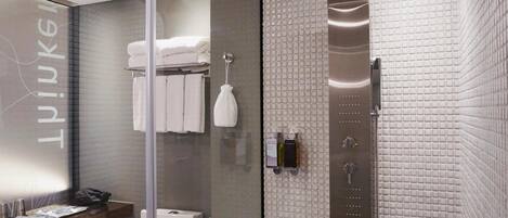 A modern bathroom with a glass shower enclosure, a towel rack with folded towels, and a wall-mounted toilet paper holder.