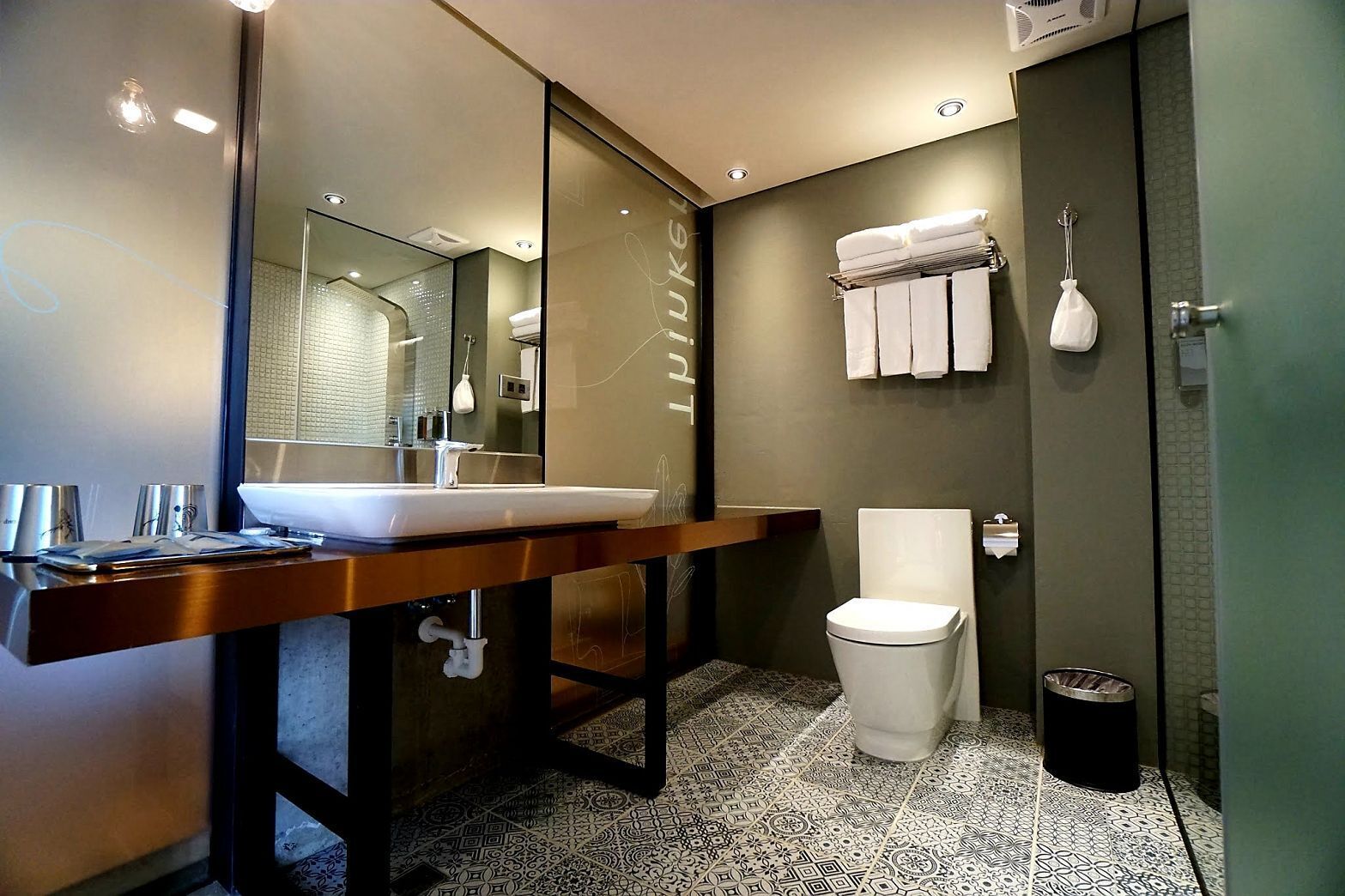 Une salle de bain moderne avec un grand miroir, un lavabo, des toilettes et une poubelle.