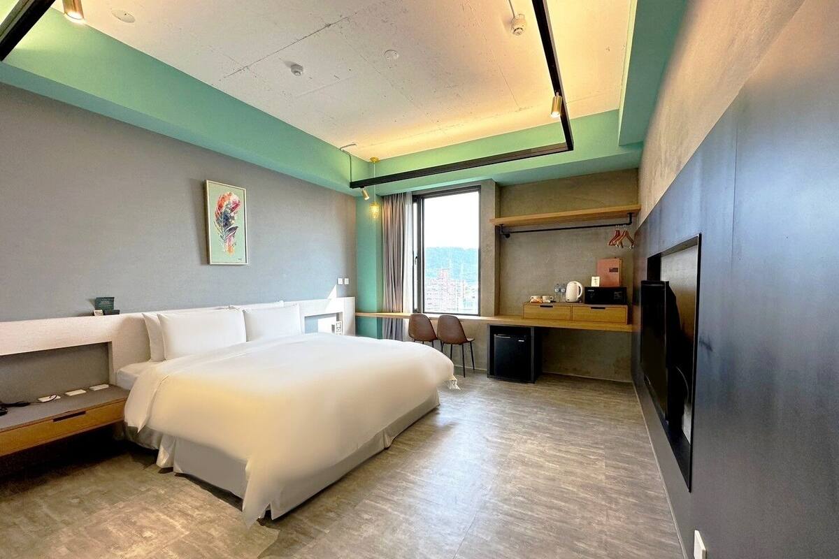 Quarto de hotel moderno com uma cama grande, uma escrivaninha, uma televisão e vista para a cidade.