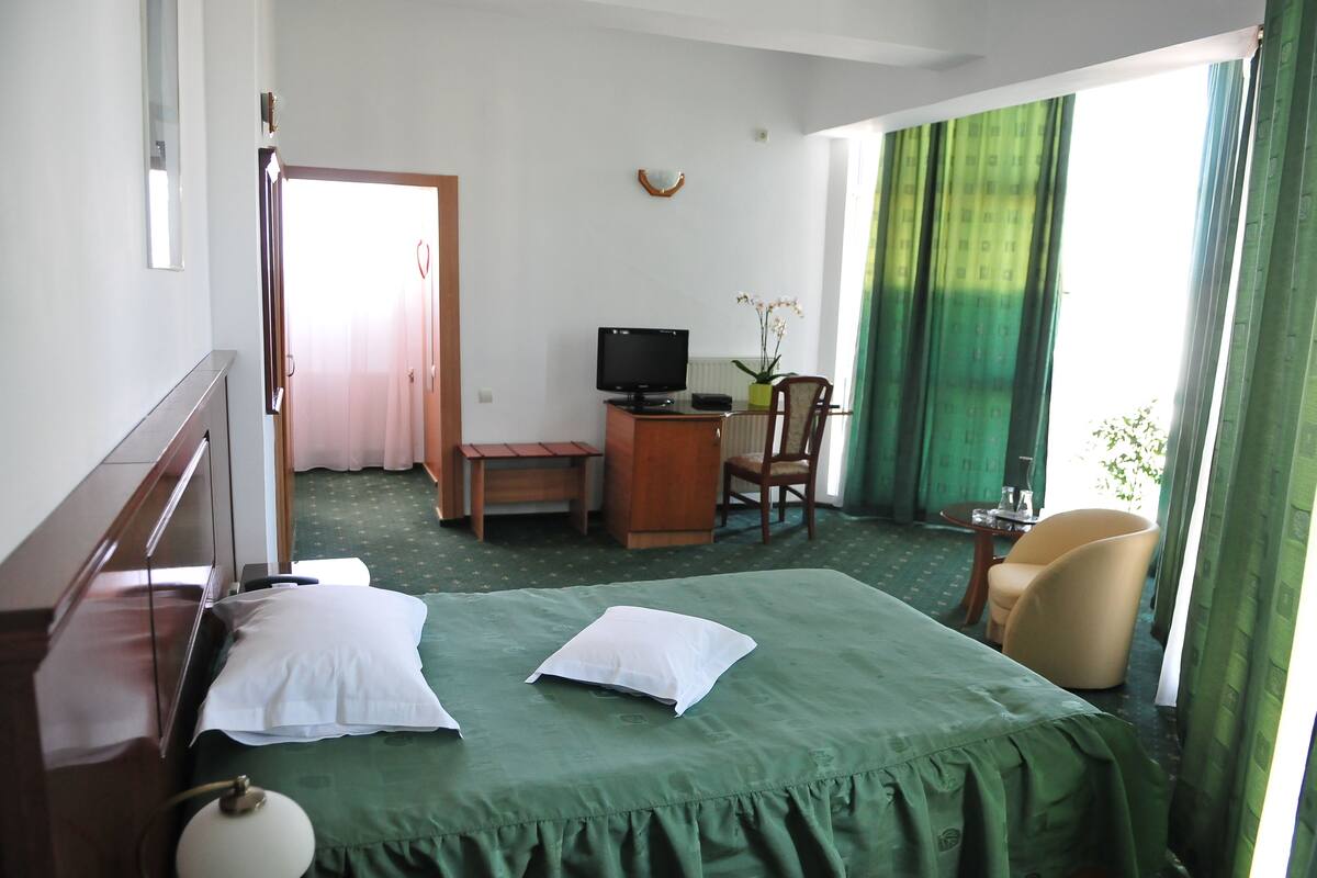 A hotel room with a bed, a desk with a computer, a chair, and a window with curtains.