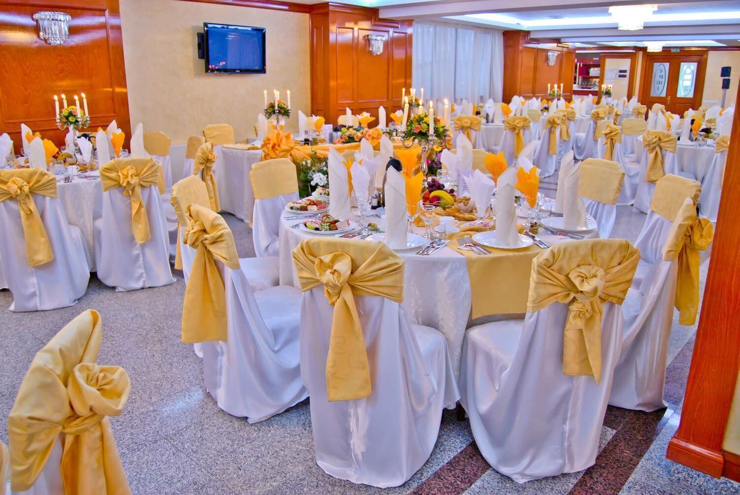 A banquet hall with round tables set for a formal event, each with white tablecloths and gold sashes.