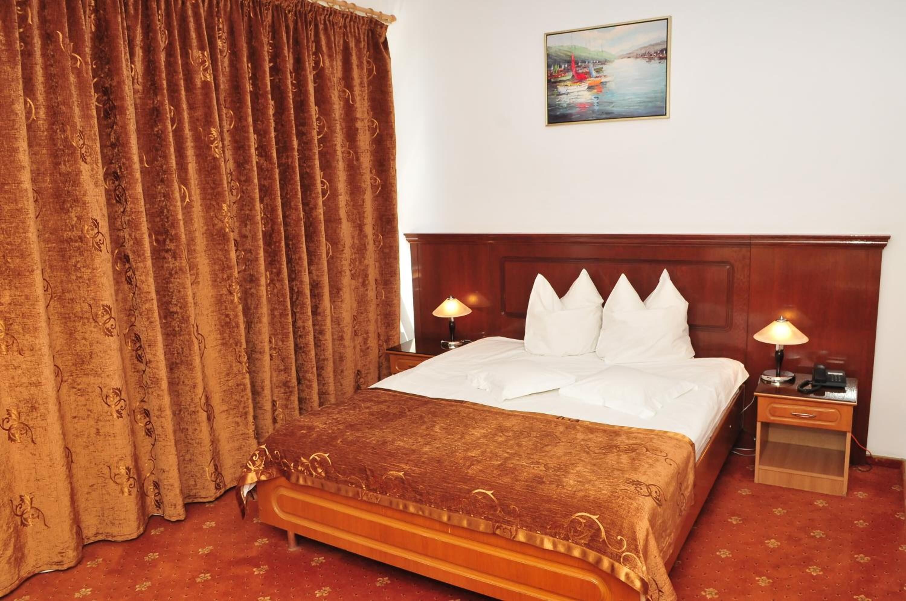 A hotel room with a large bed, two bedside tables with lamps, a painting on the wall, and a curtain.