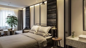 A modern bedroom with a large bed, bedside tables, a nightstand, a desk, a chair, a plant, and a bathroom with a mirror and sink. - M Do Hotel (Weifang)