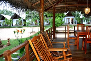 A wooden deck with seating and a view of a garden and buildings. - Hotel Riva Del Sole (Pottuvil)