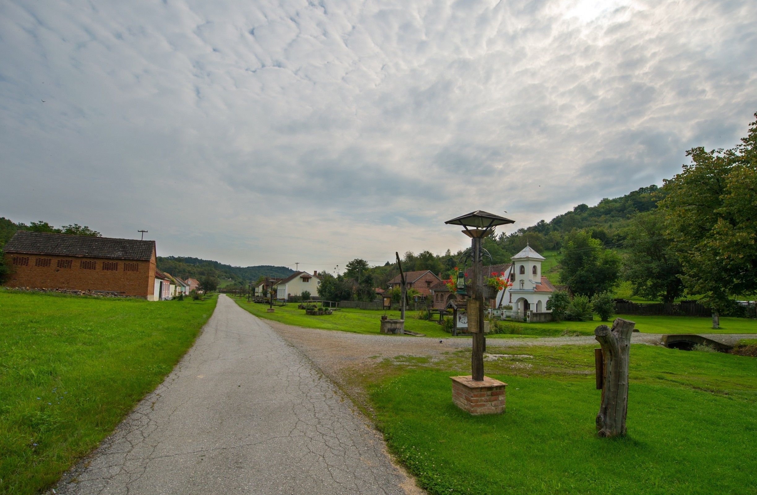 A rural road leading to a village with traditional houses, a church, and a lamppost.
