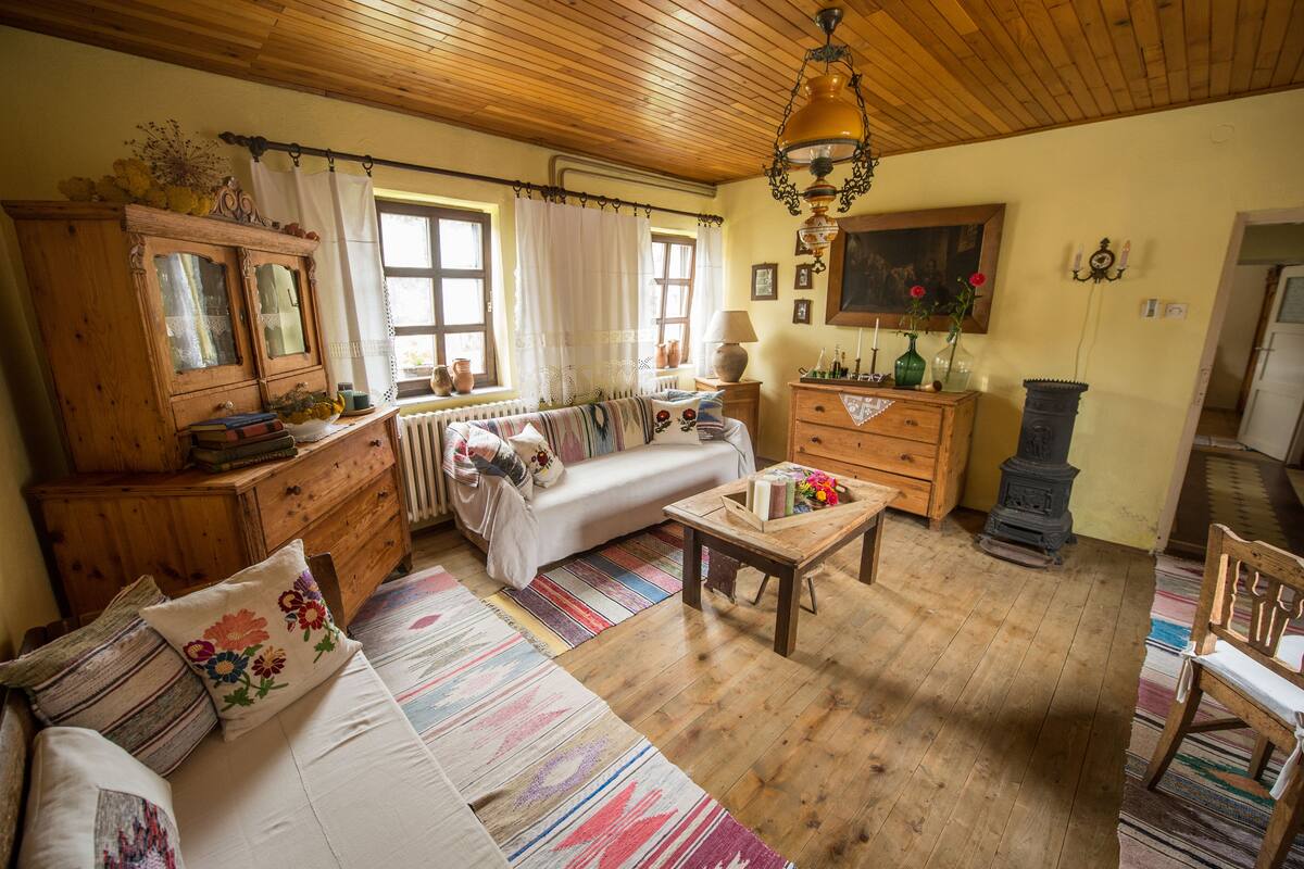 A cozy living room with a sofa, wooden furniture, a fireplace, and a window with curtains.