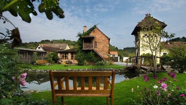 A rustic village scene with a wooden bench, a pond, and traditional houses. - Country House Stara Kapela (Nova Kapela)