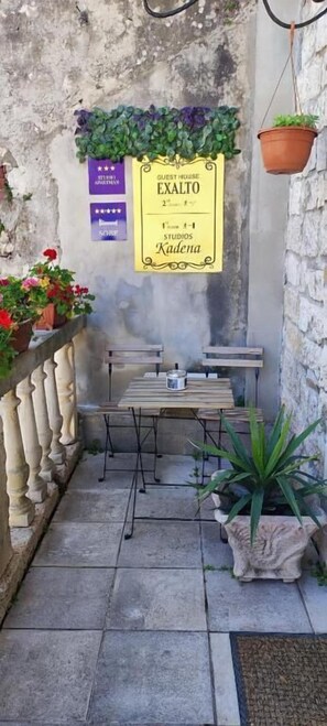 A small outdoor seating area with a table and chairs, a sign indicating 'Guest House Exalto 2nd floor', and potted plants. - Studios Kadena (Trogir)
