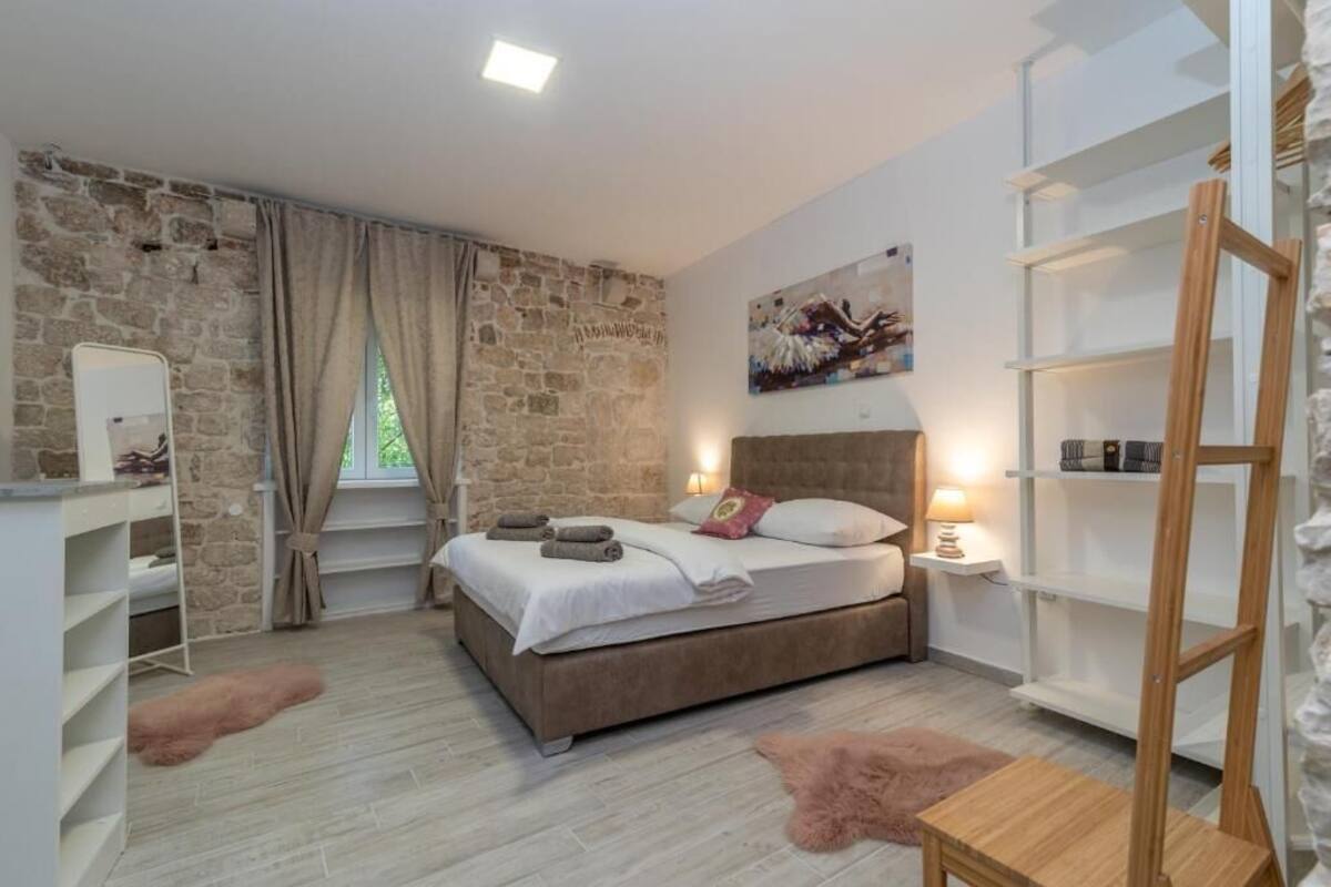 Une chambre avec un mur en pierre, un lit avec des oreillers, une table de chevet avec une lampe et une étagère en bois.