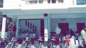 Un edificio de varios pisos con fachada blanca, balcones y una entrada a nivel de calle con motocicletas estacionadas.