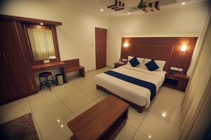 A hotel room with a large bed, a wooden desk, a chair, a small table, and a mirror. - White Portico (Peermade)
