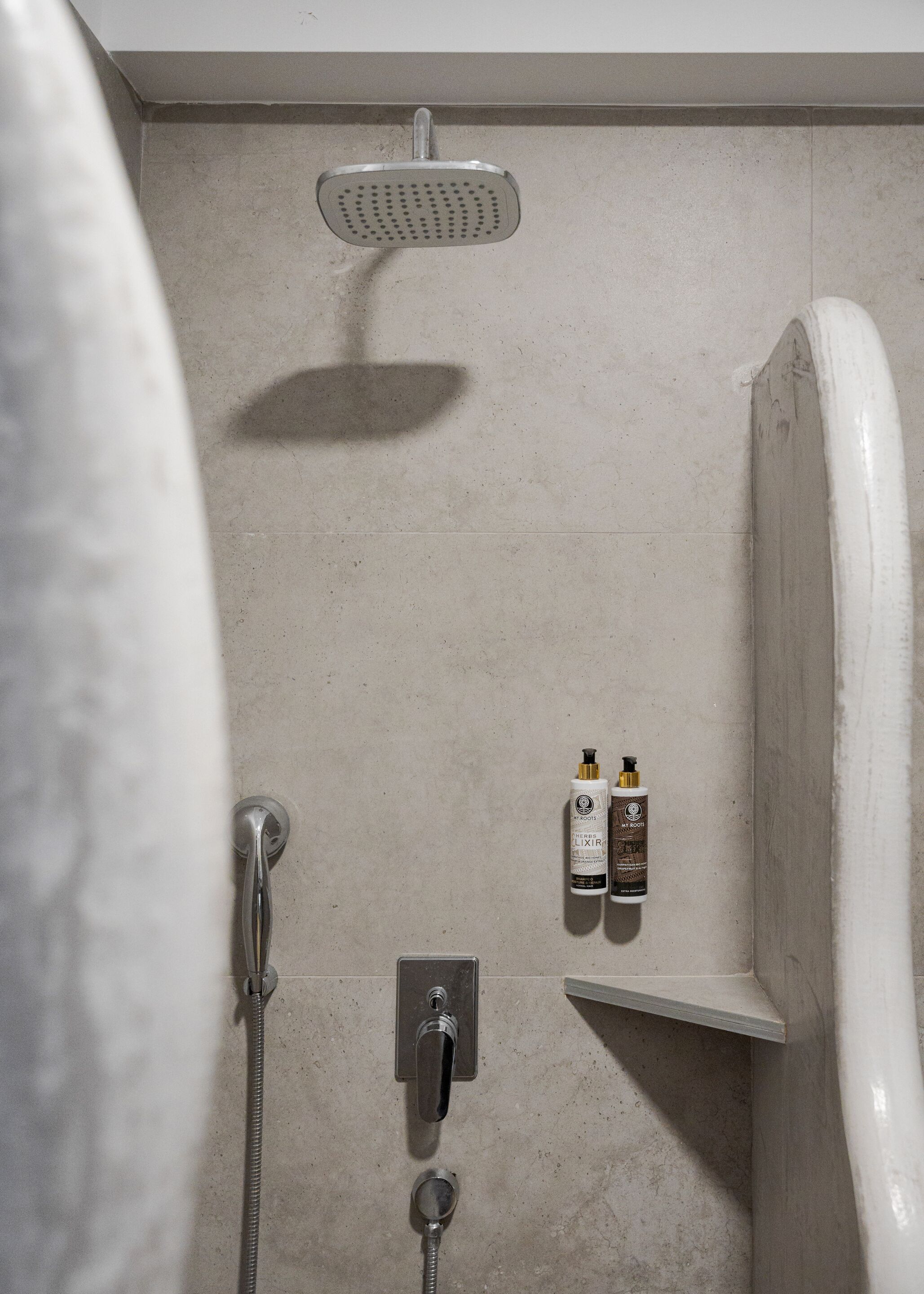 A bathroom with a shower, a towel rack, and two bottles of shampoo on a shelf.