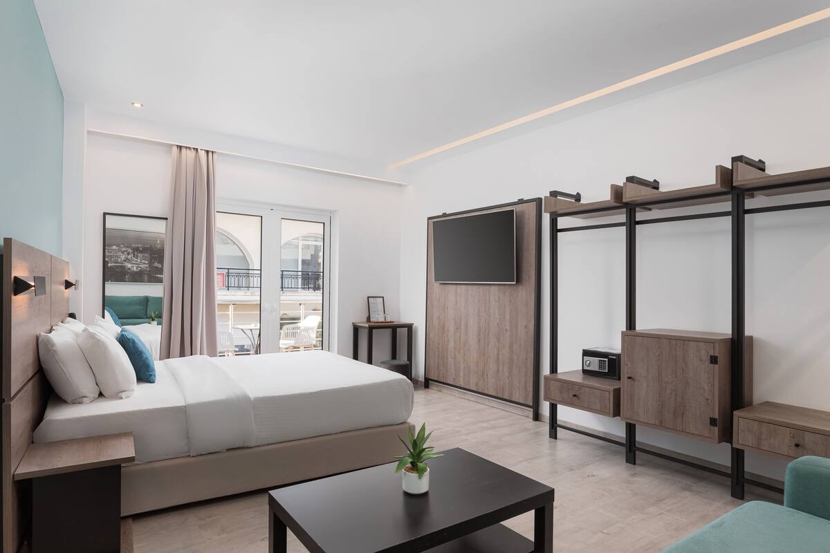 A modern hotel room with a bed, a TV, a desk, and a balcony with a view.