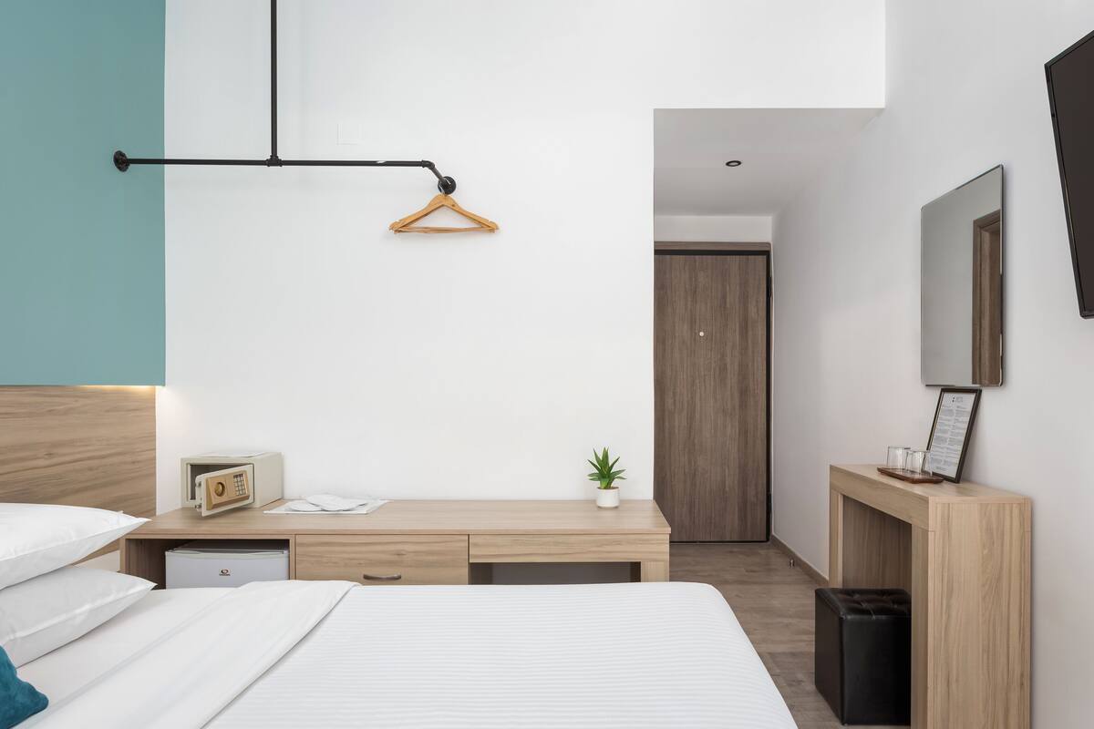 A modern hotel room with a bed, bedside table, desk, and wardrobe.