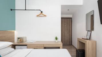 A modern hotel room with a bed, bedside table, desk, and wardrobe.