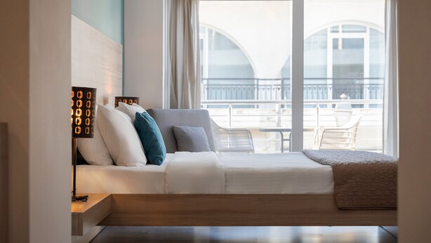 Une chambre d’hôtel moderne avec un canapé-lit, une table de chevet, une lampe et une vue sur le balcon.