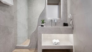 Une salle de bain moderne avec une douche à parois courbes, un lavabo intégré et un miroir. On y trouve un porte-serviettes et une petite plante posée sur le lavabo.