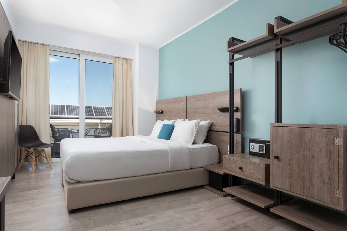 A hotel room with a bed, a desk, a chair, a wardrobe, and a TV.