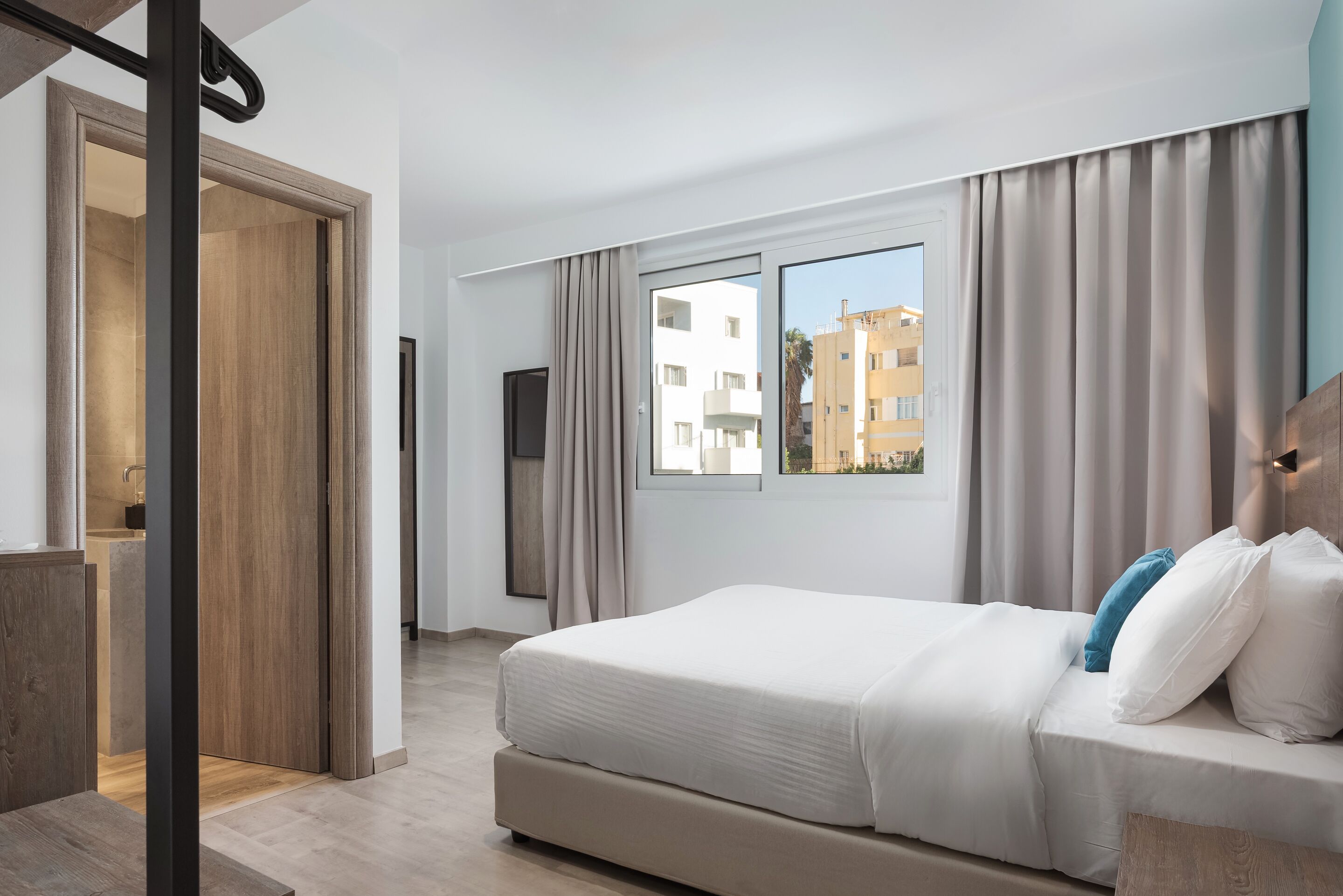 A modern hotel room with a large bed, a TV, and a window with curtains.