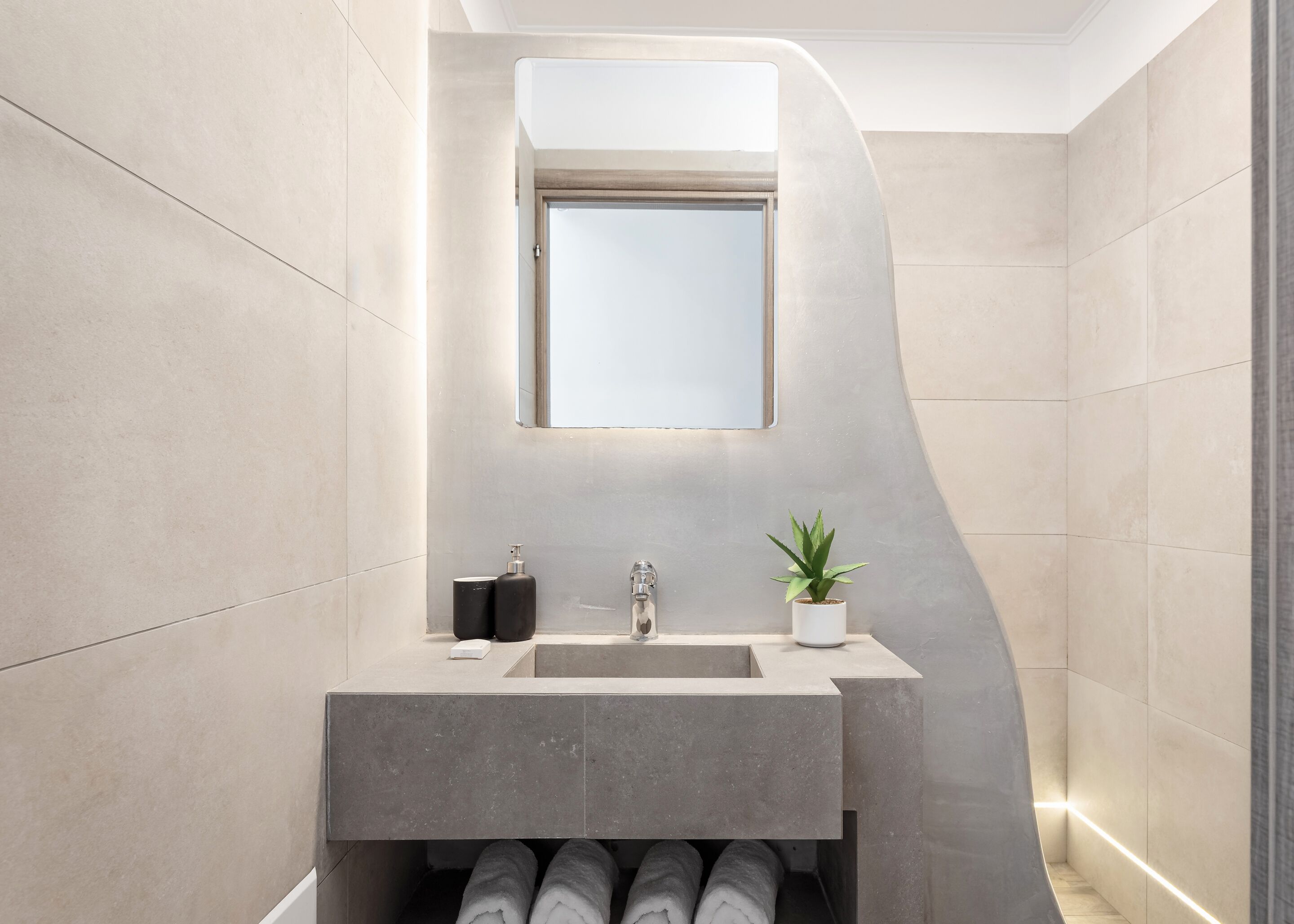 A modern bathroom with a large mirror, a sink, and a potted plant.