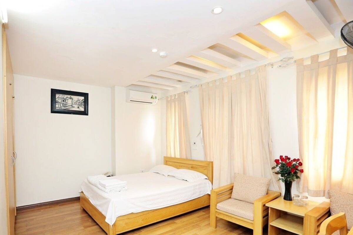 A hotel room with a wooden bed, a chair, a small table, and a window with curtains.