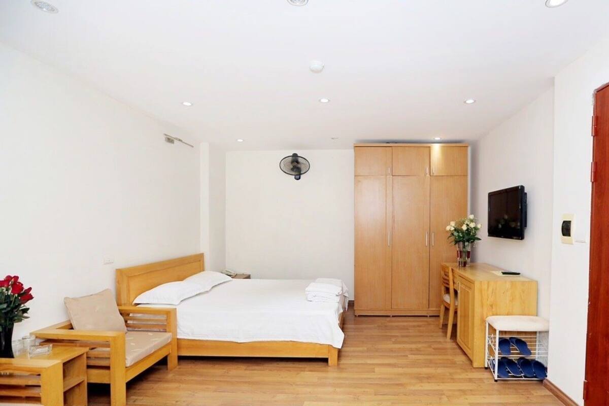 A bedroom with a wooden bed, a wooden chair, a wooden desk, a TV, and a wardrobe.