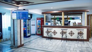 Zona bar con un bancone, sgabelli, distributori automatici e un frigorifero.