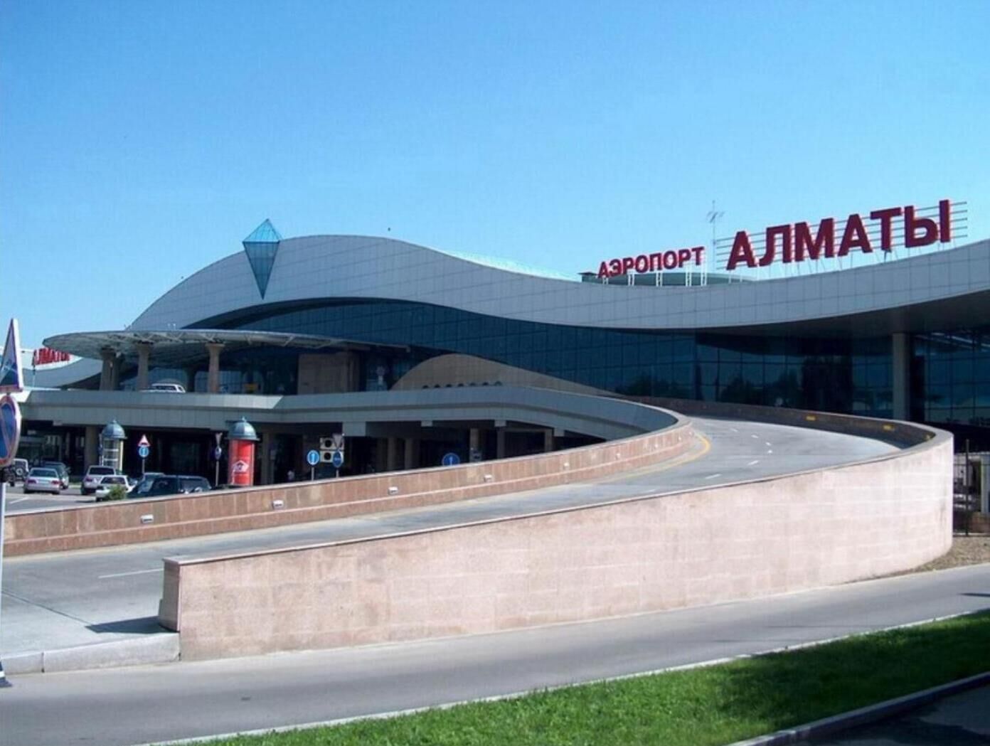 Una moderna terminal de aeropuerto con techo curvo y el letrero 'Аэропорт АЛМАТЫ'.