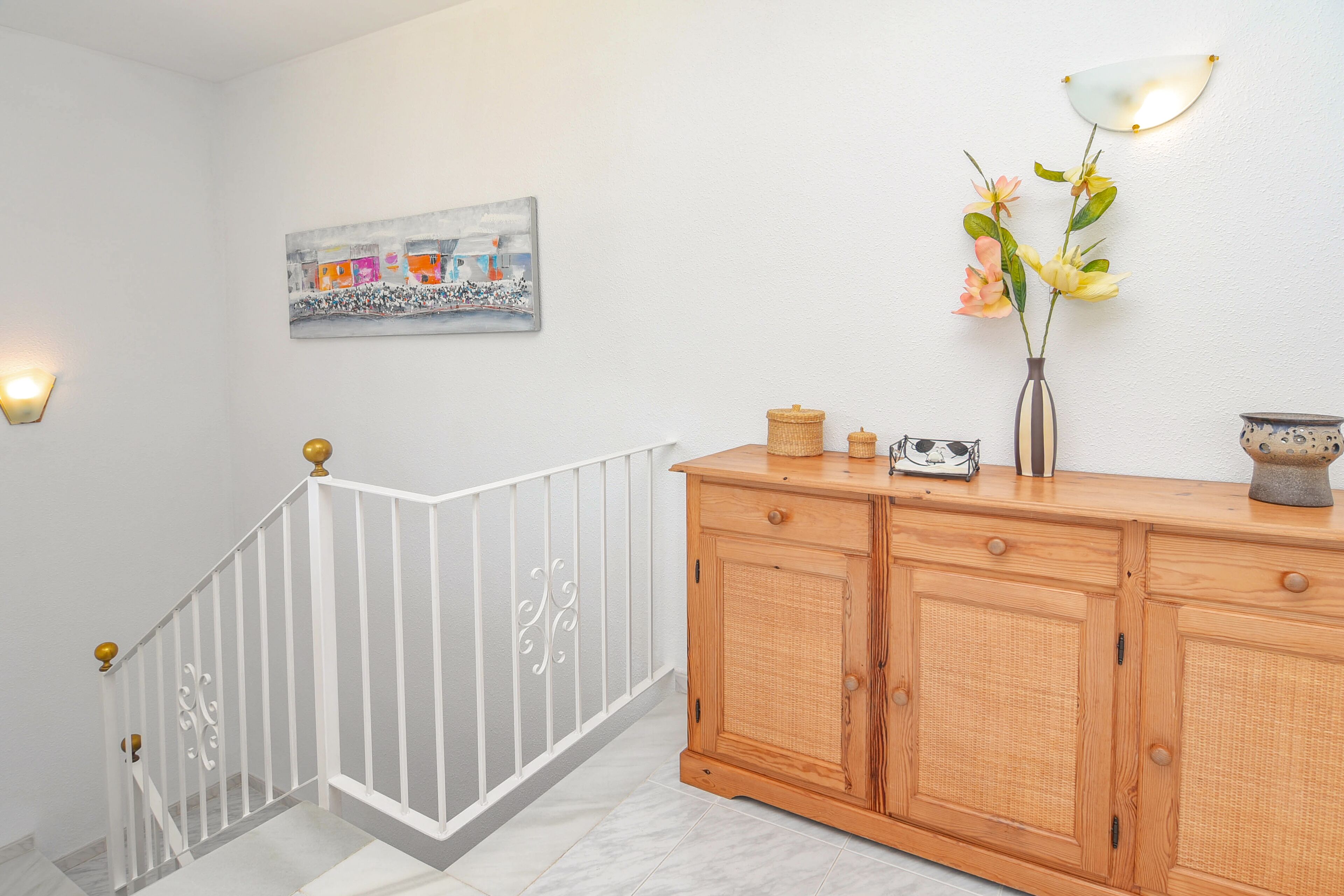 Una escalera con barandillas blancas y un aparador de madera con un florero.
