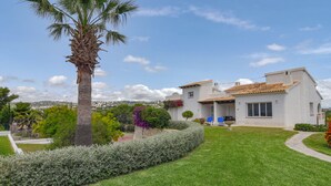 A two-story house with a tiled roof, surrounded by a well-maintained lawn and a palm tree. - Lucy Moraira House for 6 people (Moraira)
