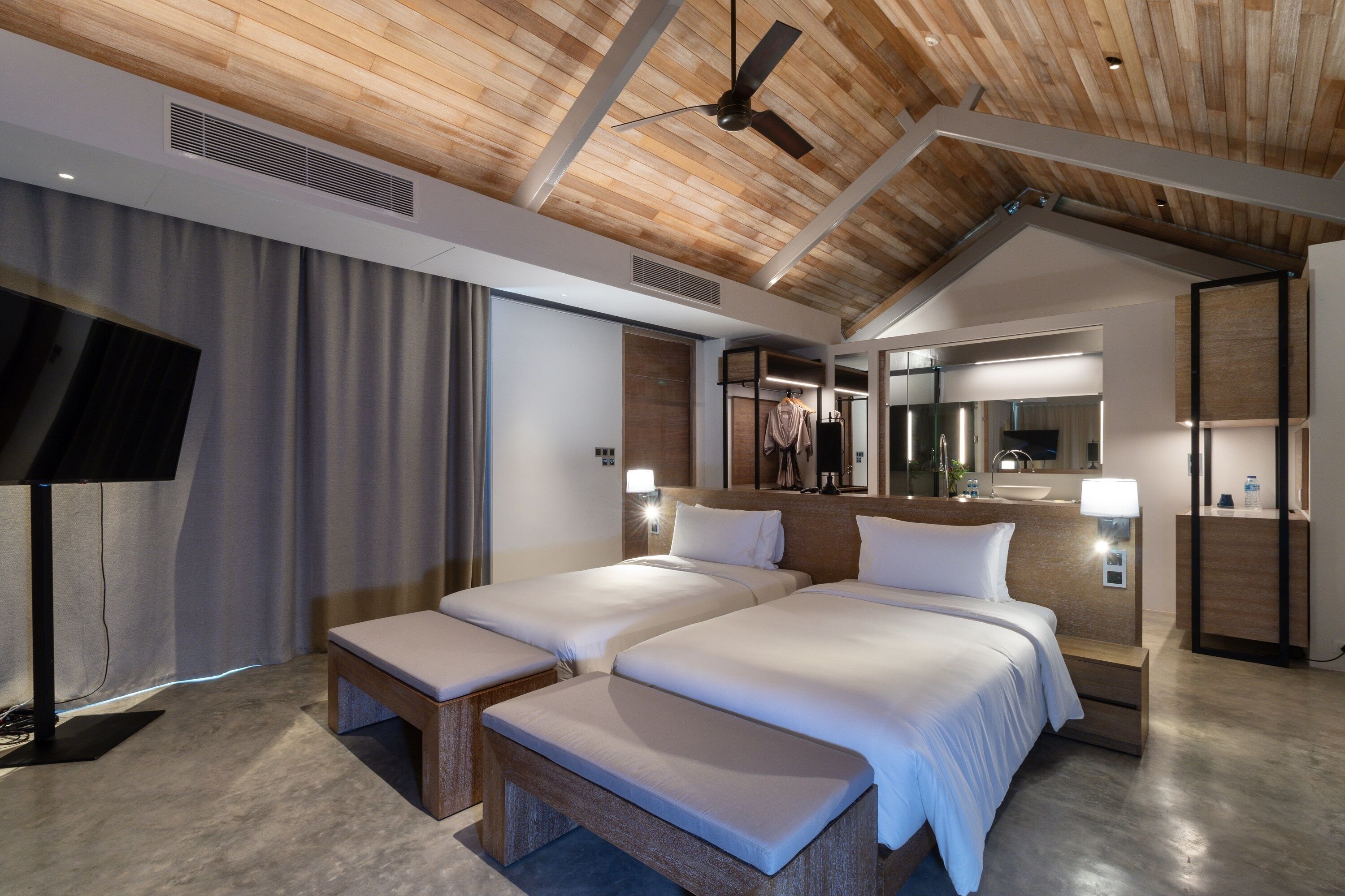 A modern hotel room with a sloped ceiling, two beds, a television, and a large mirror.