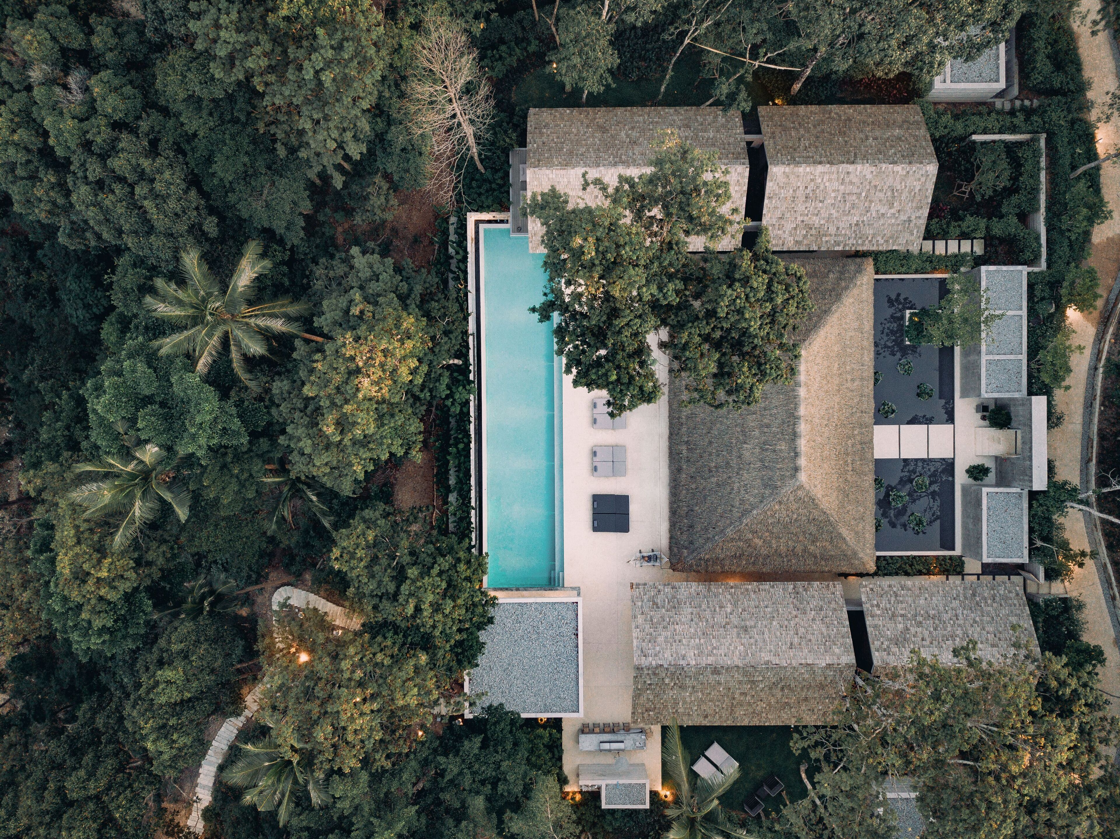 Vista aérea de un complejo turístico con piscina, varias edificaciones y abundante vegetación.