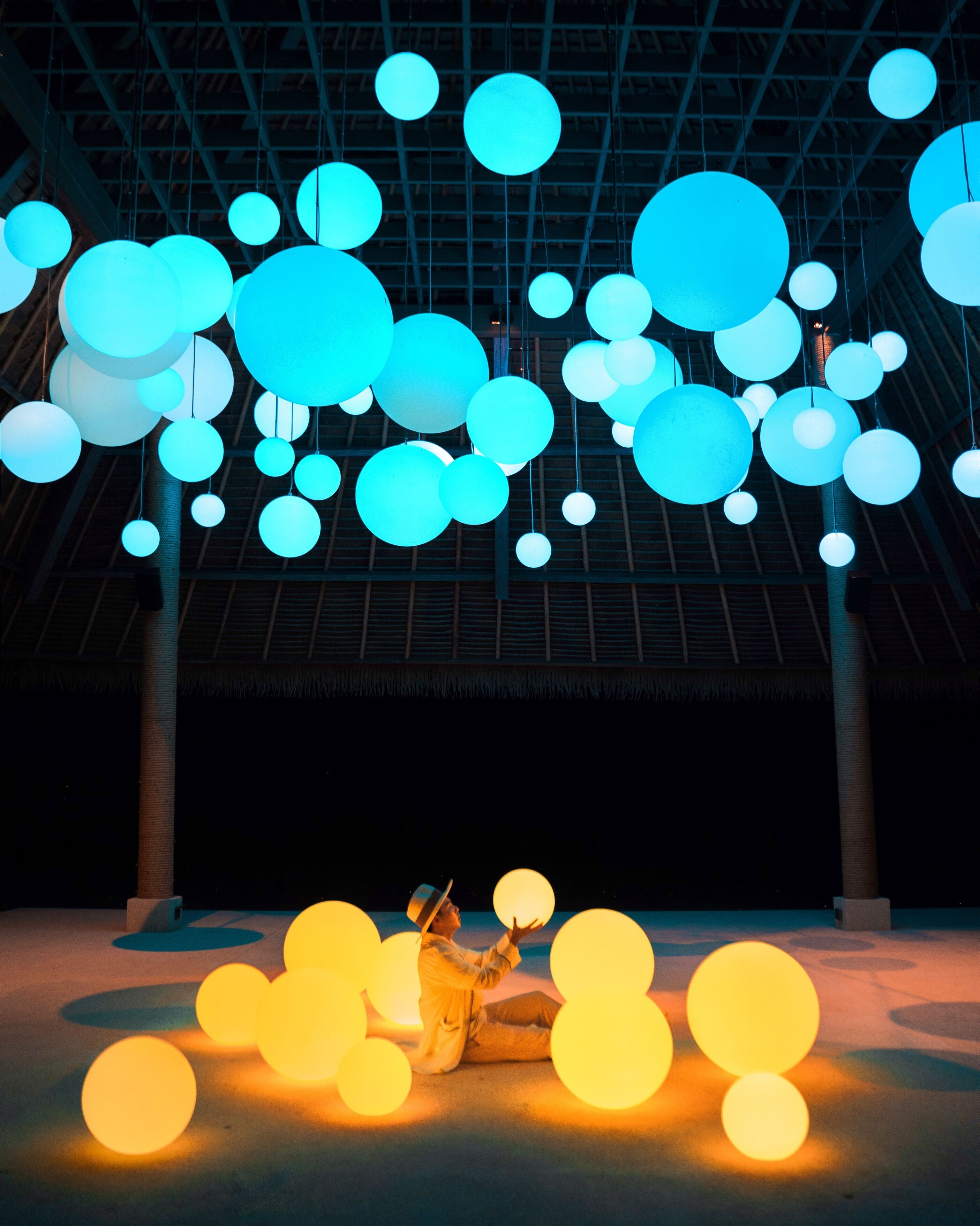 A large indoor space with a high ceiling, featuring numerous spherical light fixtures in blue and yellow.