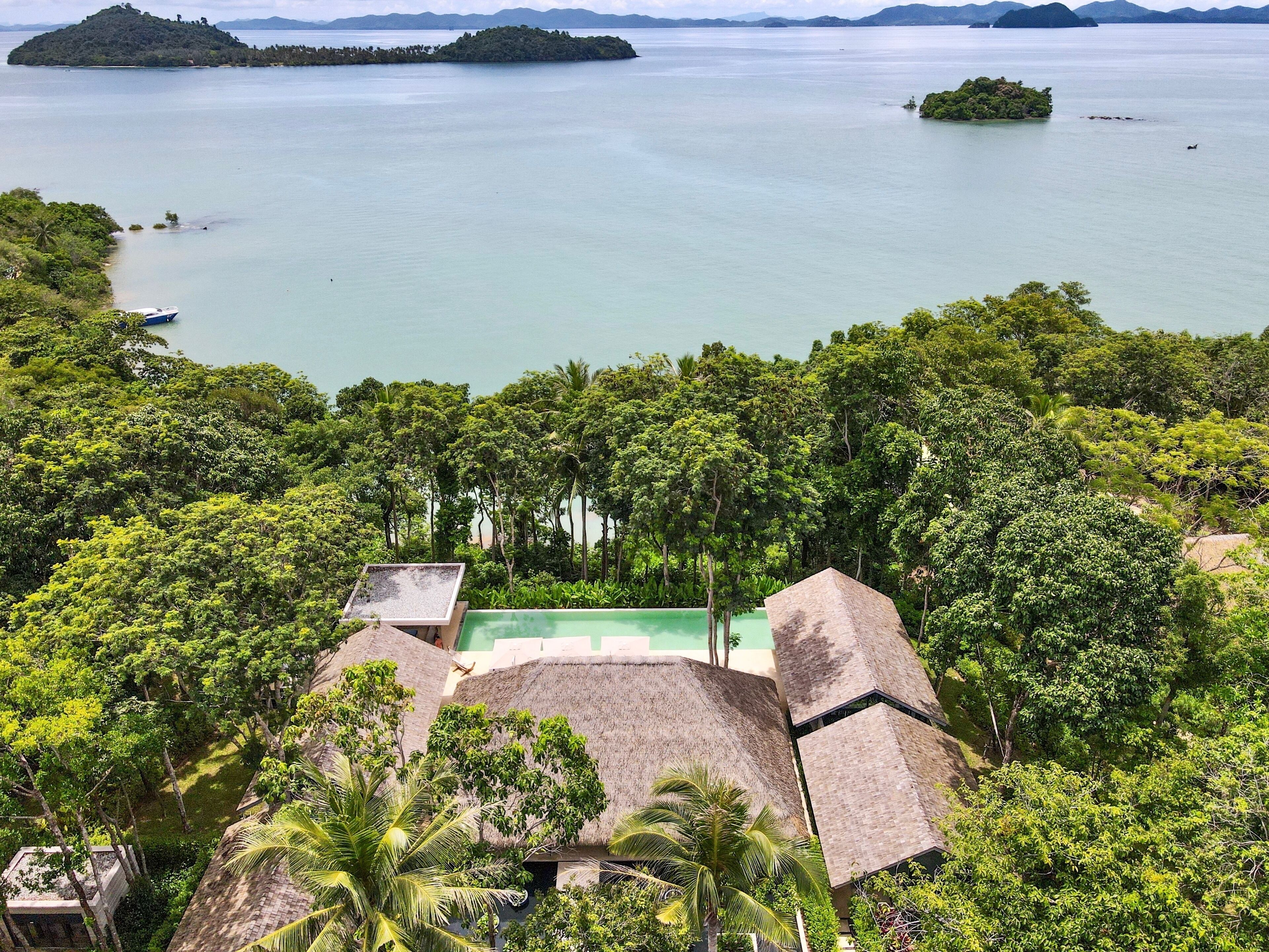 Ein tropisches Resort mit strohgedeckten Gebäuden, üppiger Vegetation und Blick auf das Meer und die Inseln.
