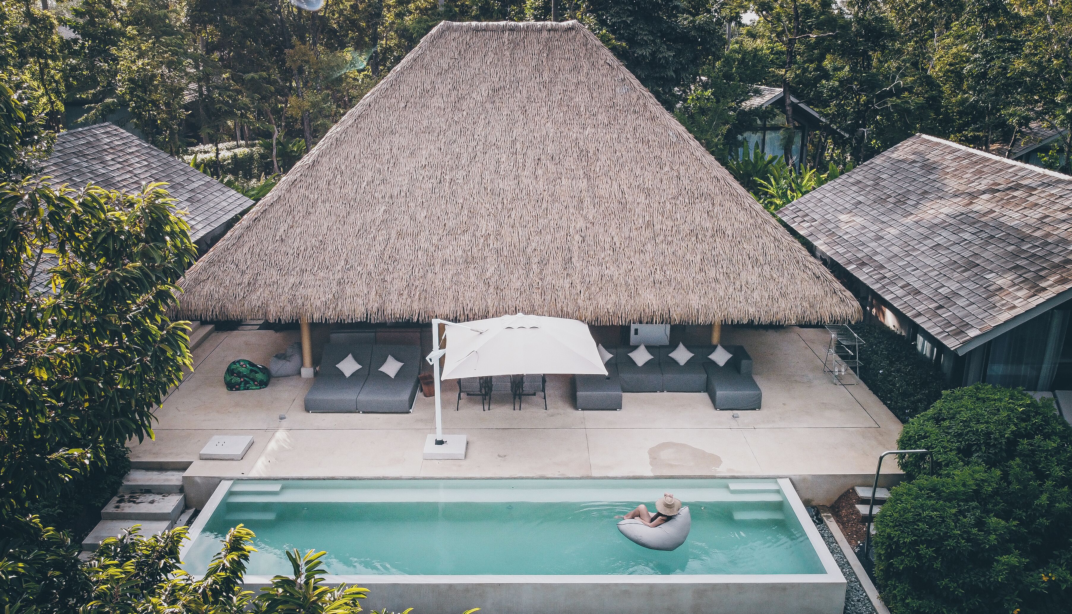 Un resort con una estructura de techo de paja, piscina y zonas de descanso.