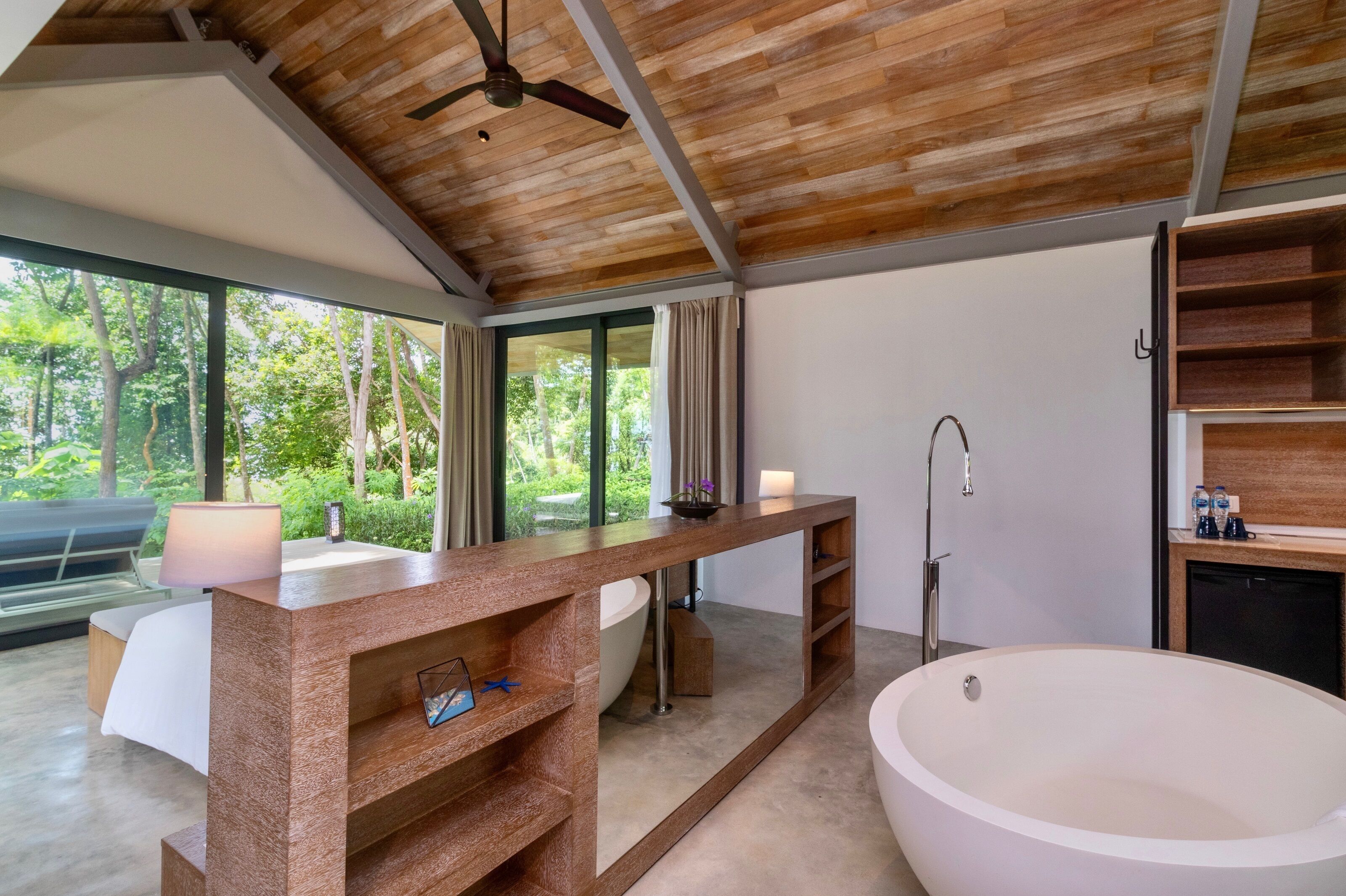 Ein modernes Badezimmer mit einer großen Badewanne, einem Holz-Waschtisch und einem großen Fenster mit Blick auf Grünflächen.