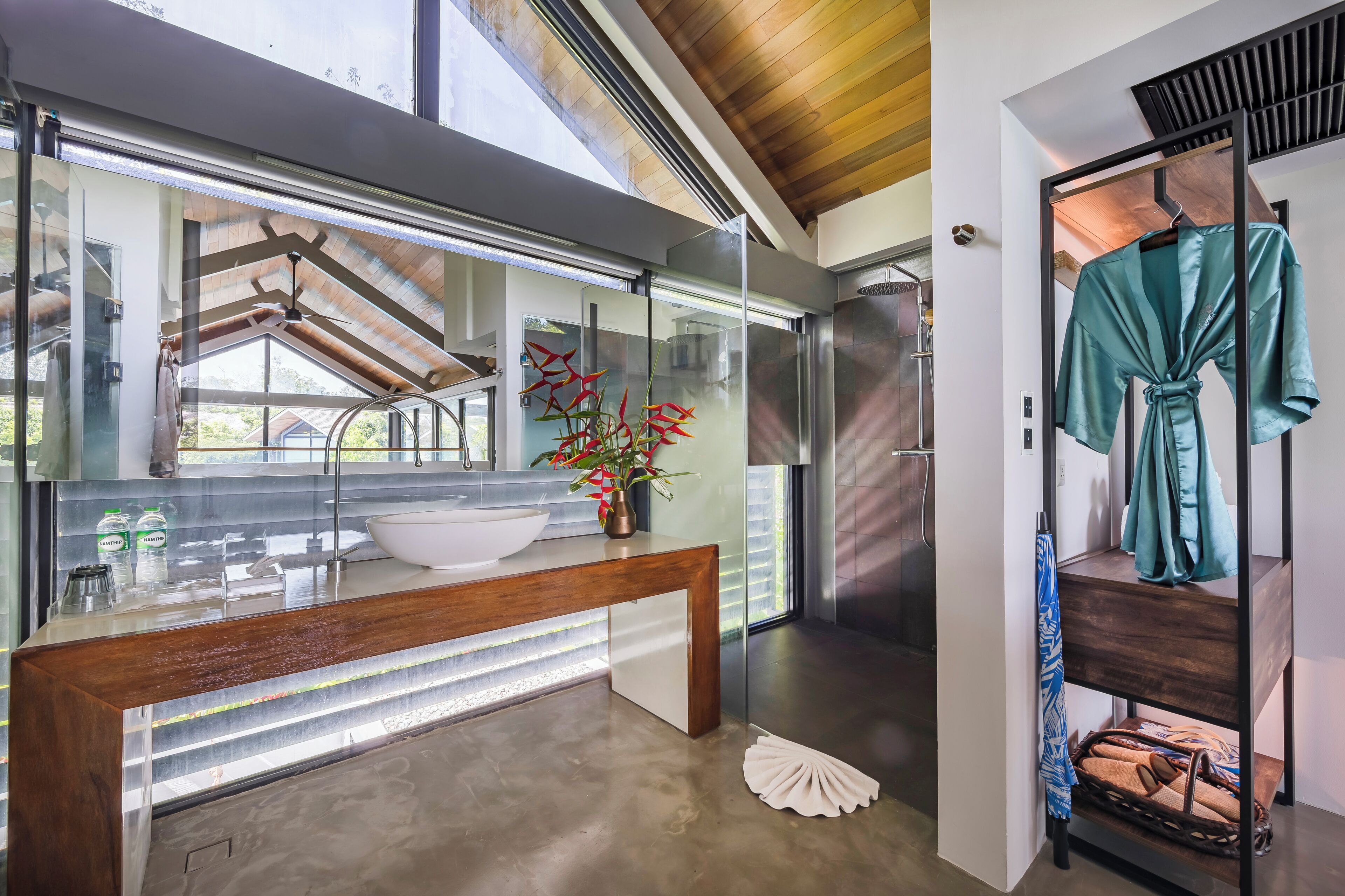 Un baño moderno con un espejo grande, un tocador de madera, un lavabo blanco y una planta en maceta.