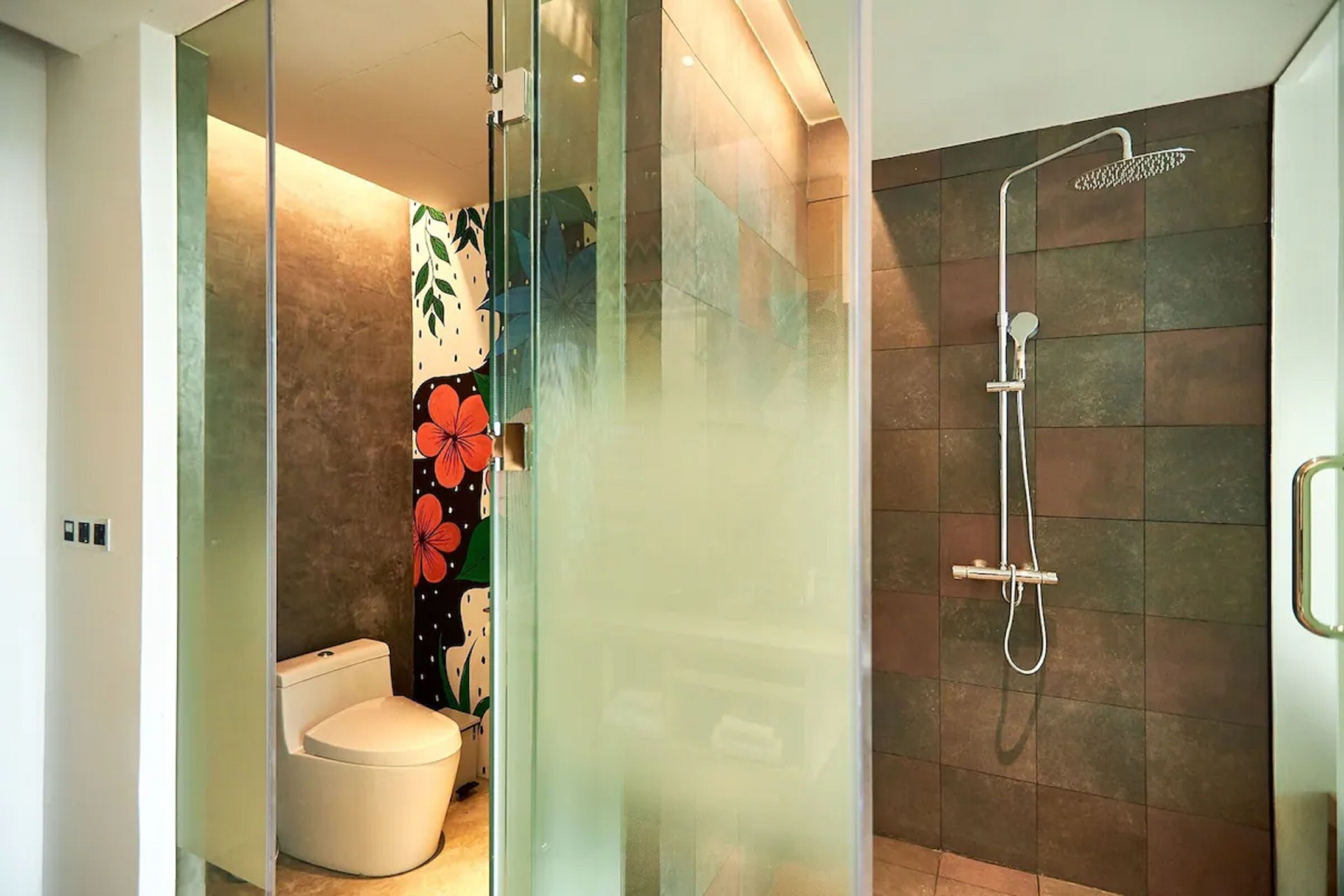 A modern bathroom with a glass partition, a toilet, and a shower area with a handheld showerhead.
