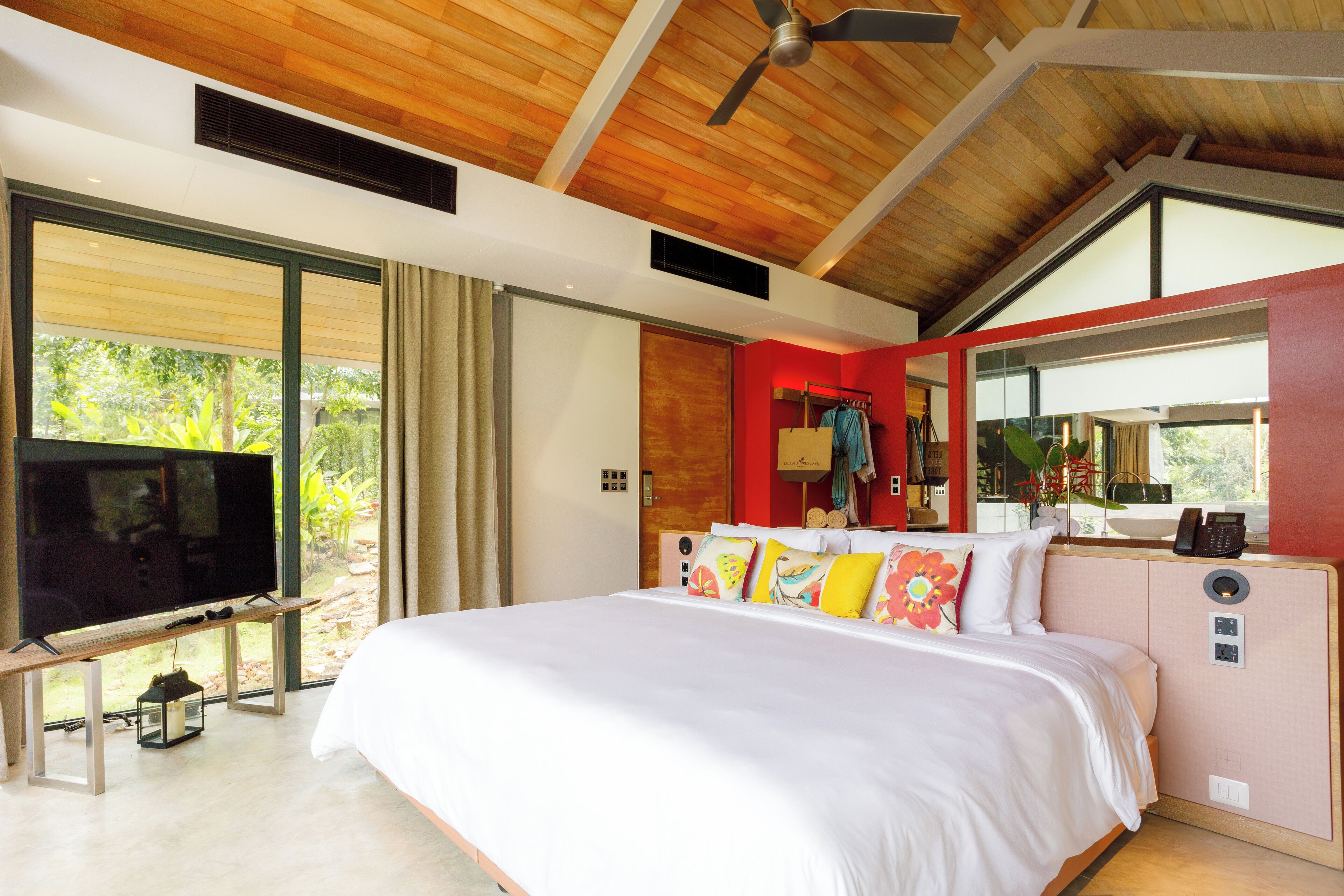 Une chambre moderne avec un grand lit, un téléviseur posé sur un meuble en bois et une vue sur la verdure.