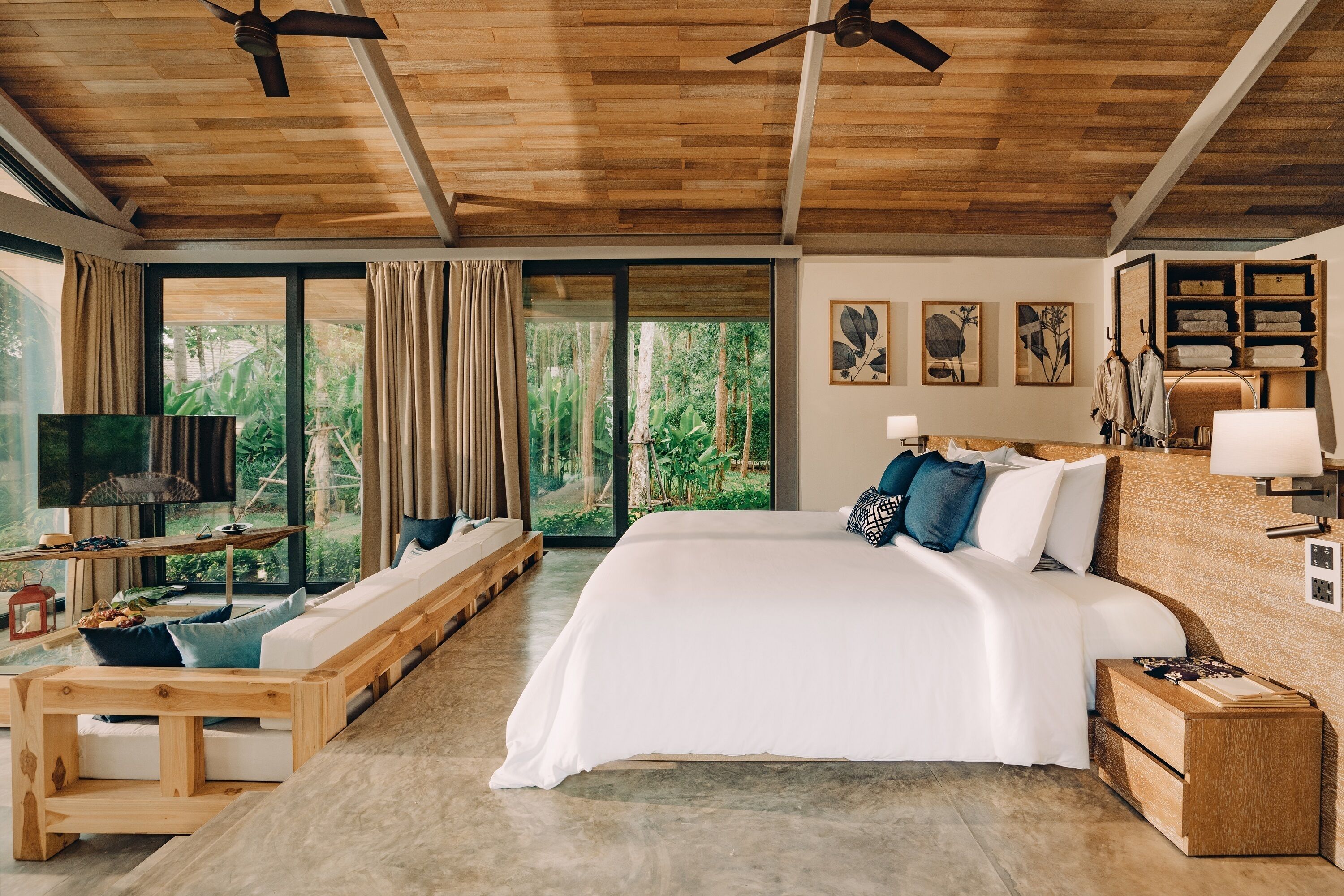 A spacious bedroom with a large bed, wooden ceiling, and a view of the outdoors through large windows.