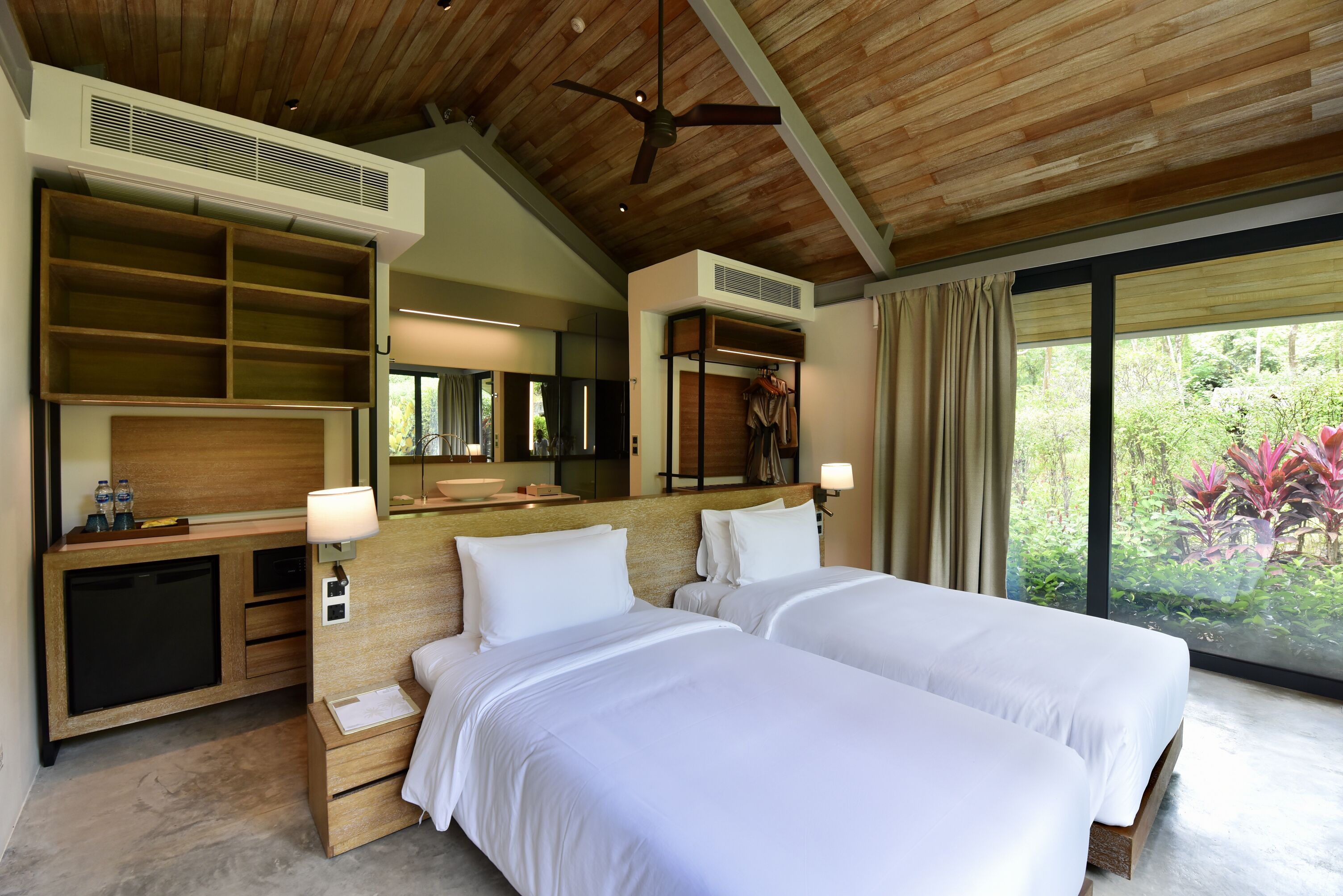 Habitación de hotel con dos camas, un escritorio, un espejo y un ventanal con vistas a zonas verdes.