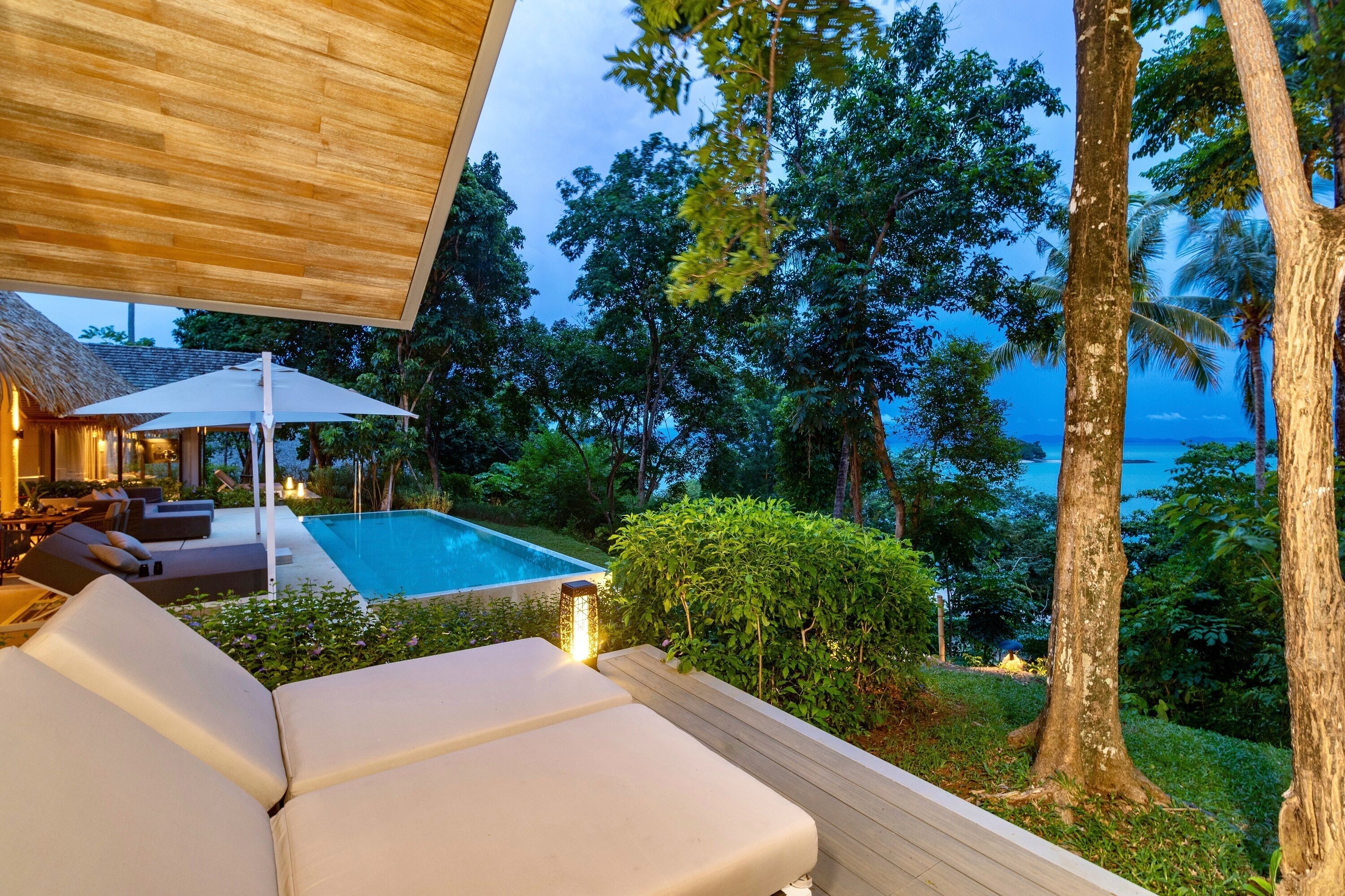 A poolside area with lounge chairs, a wooden deck, and a view of the ocean.